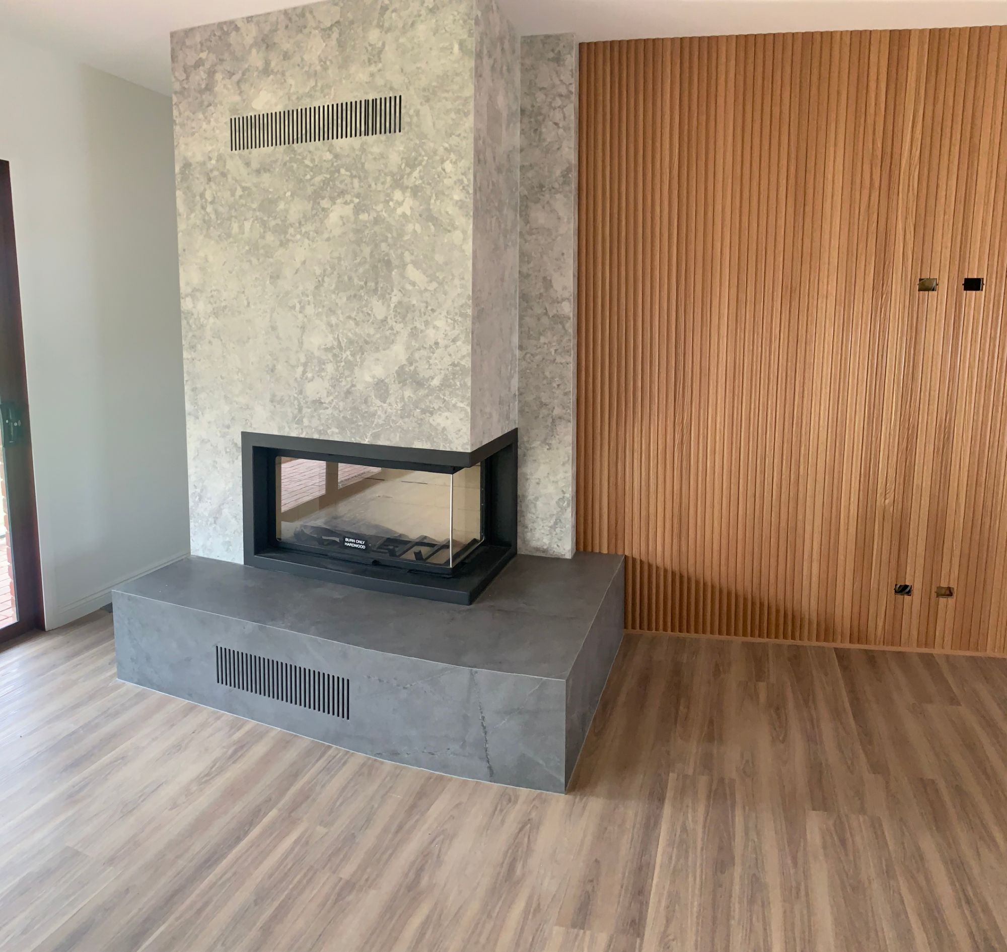 Corner fireplace with stone surround beside a timber batten feature wall